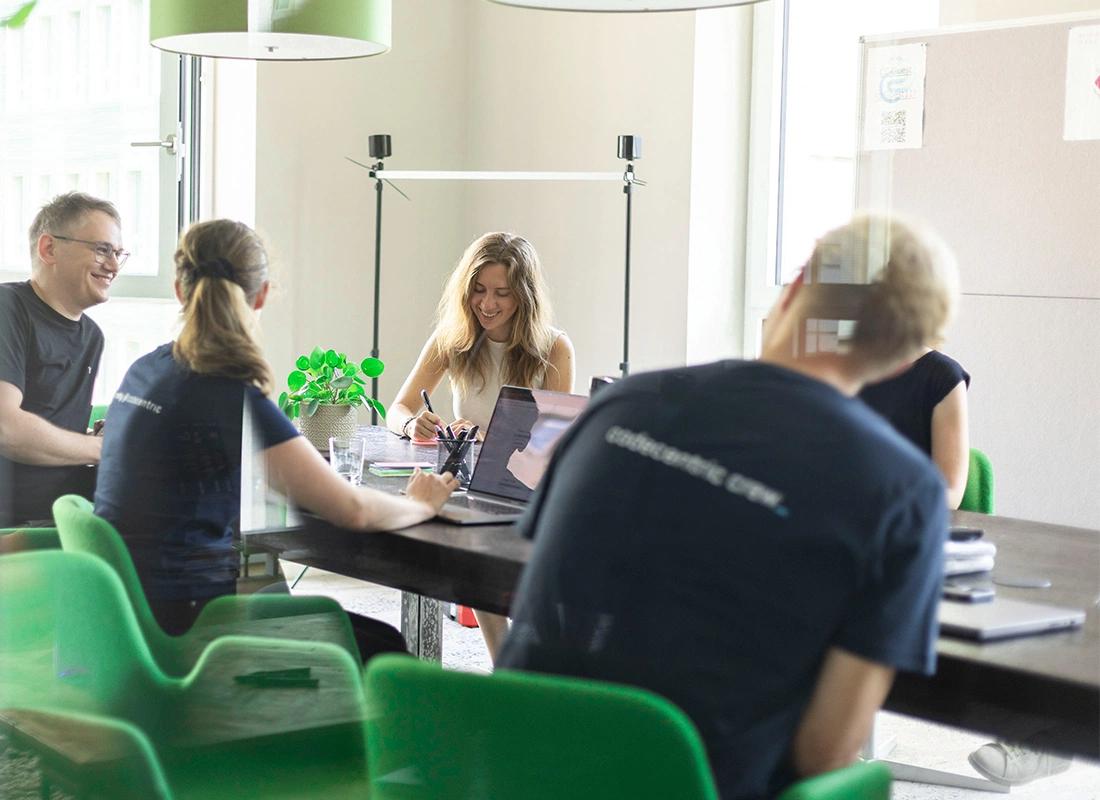 Menschen sitzen um einen Tisch herum, lächeln und arbeiten zusammen