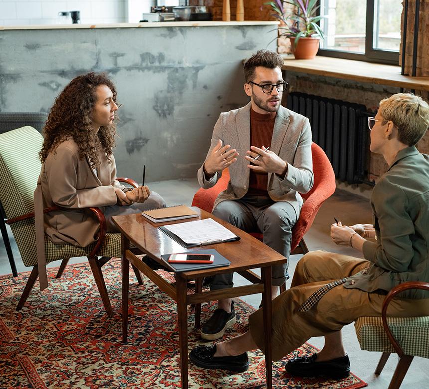 Drei Personen sitzen um einen gemütlichen Tisch herum und diskutieren zusammen über ein Projekt