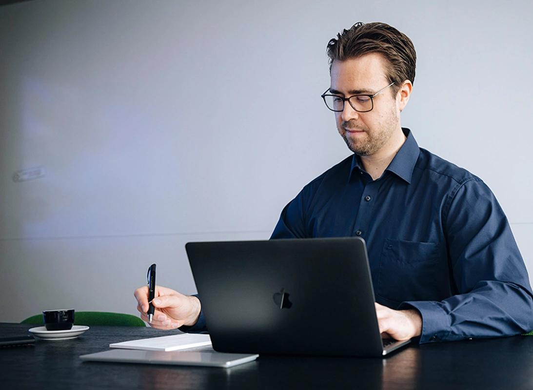 Mann sitzt am Tisch und arbeitet gleichzeitig am Computer, Tablet und mit Stift und Papier.