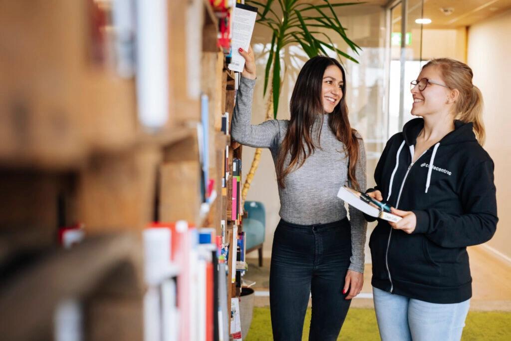 Jenny steht mit einer Kollegin an einem Bücherregal bei codecentric.